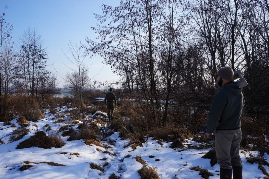 A person stands in a snowy field with a cinderblock on their shoulder while a second person walks ahead.