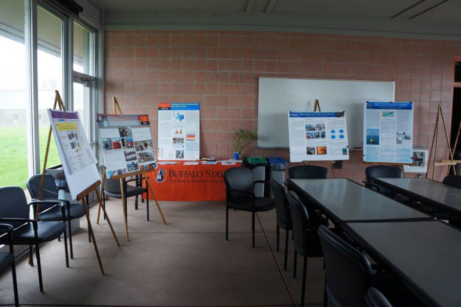 Posters set up on easels in an empty room with some long tables and chairs at the table and along the windows at the edge of the room.