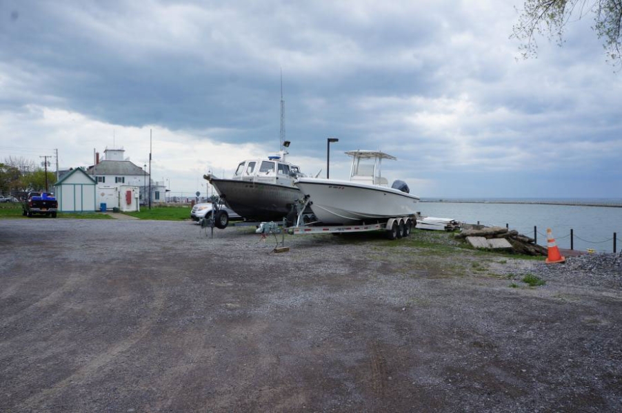 two boats parked on trailers in a parking lot by the water