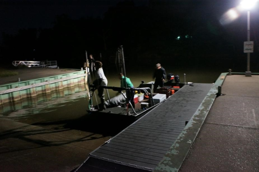 Nighttime picture of a boat sitting in the water at a boat launch. Three people are on board.