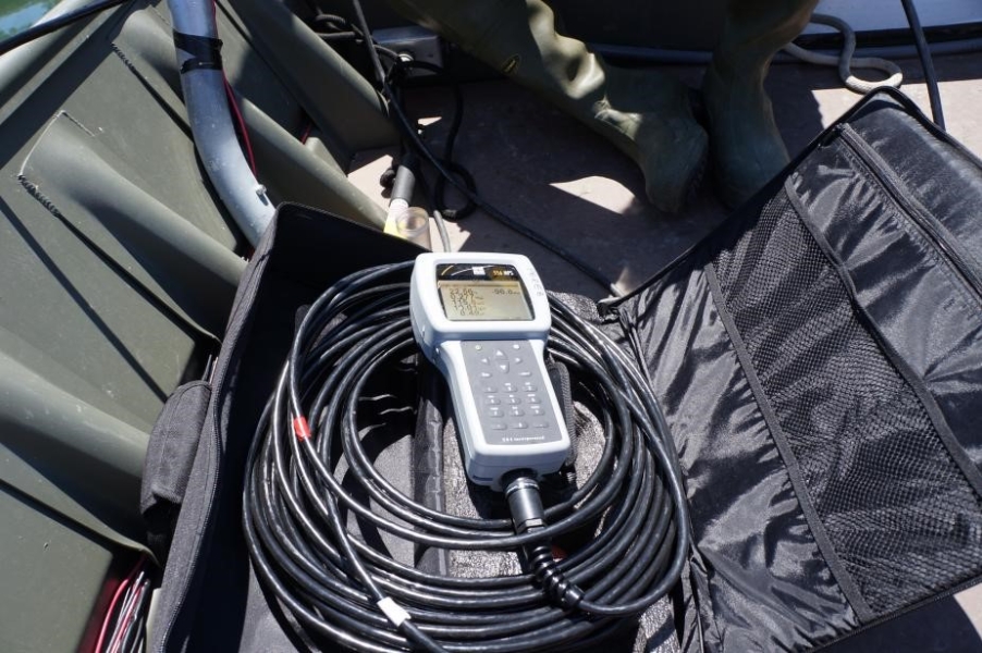 A sampling instrument with a screen sits on a coil of cable in an open case on a boat.