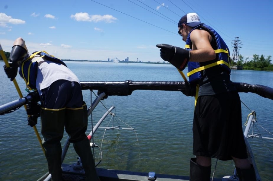 Two people lean over a railing at the front of a boat with long poles.