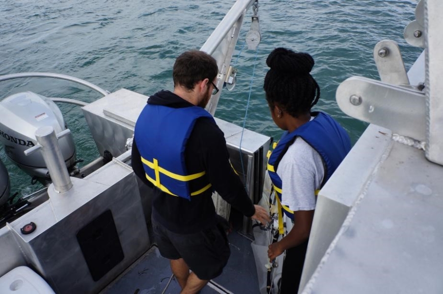 Two people in life jackets stand by the edge of a boat