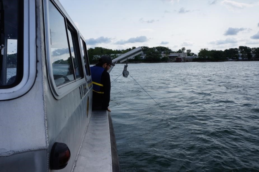 A person near the edge of a boat looks toward a rope going into the water