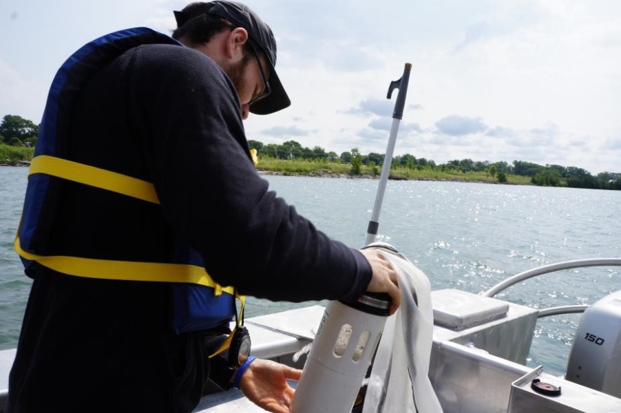 A person on a boat holds a plastic bottle at the end of a net