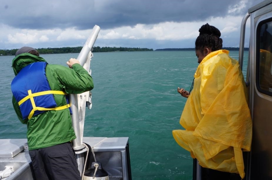 Two people in rain gear stand by the edge of the boat. One is near a winch and the other has a stopwatch