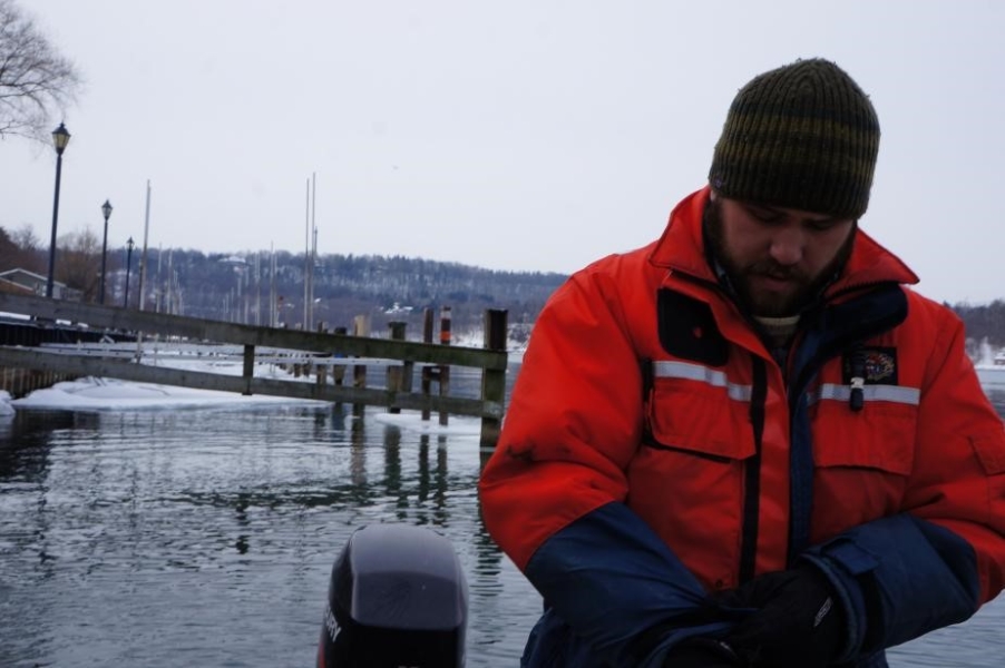 a person in a flotation suit and knit cap stands by the icy water near a marina