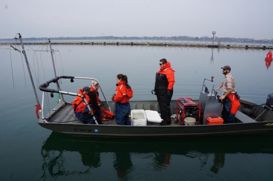 Students on a shallow boat with railings and two booms. Someone is operating the boat.