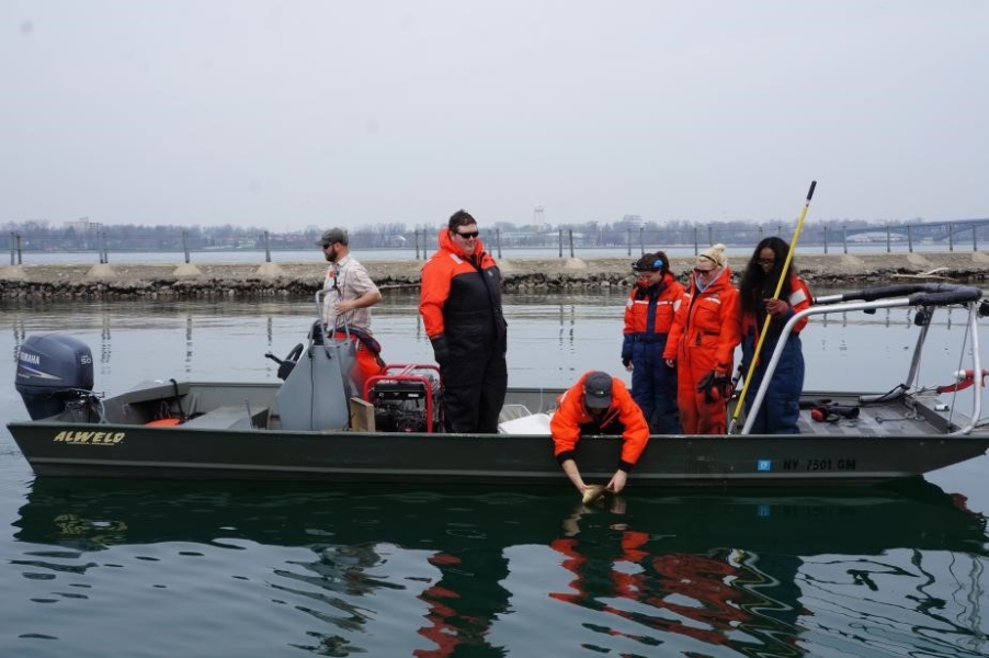 People standing on a shallow boat. One person holds a net with a long pole while another student leans over the edge to release a fish back into the water