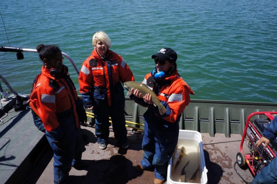 A person on a boat holds a fish while two others stand nearby.