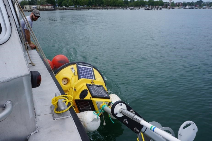 A person leans over the side of a boat to look at a buoy tied up alongside the boat as they move out of port.