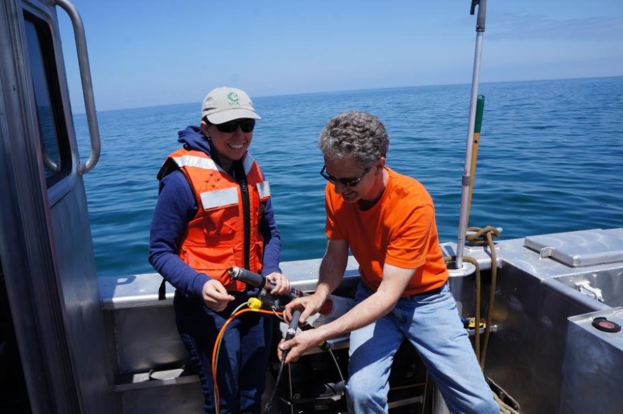 Two people in the back of a boat. One is holding a cable and the other is holding a cylindrical instrument.