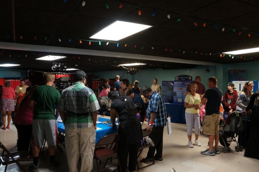 Groups of people visiting different display tables in a room.