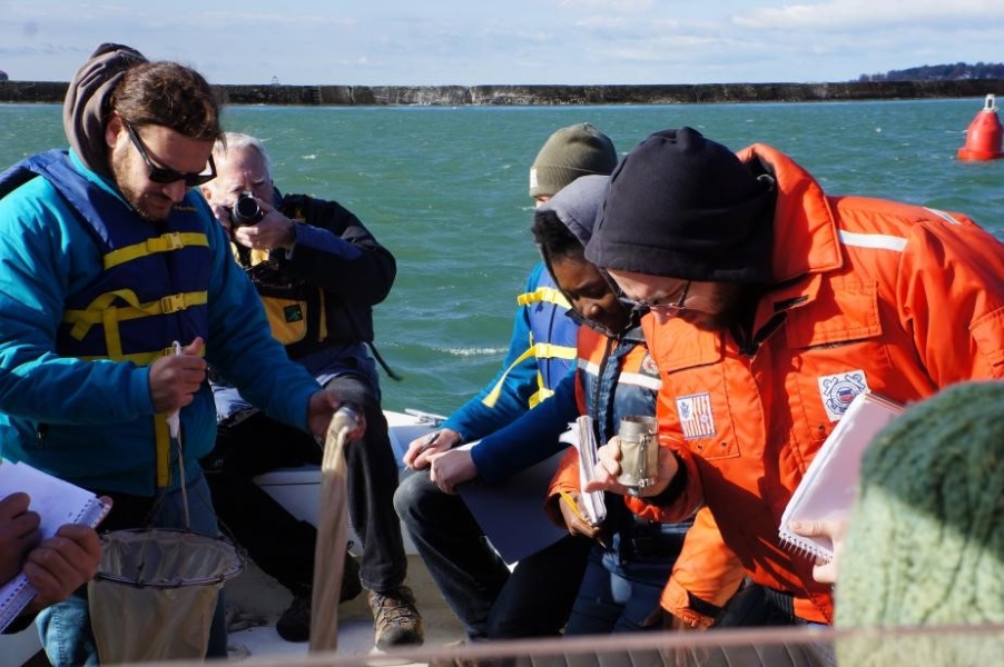 Several people on a boat. One is holding something in their hand and looking at it, and an older person at the back is taking a picture.