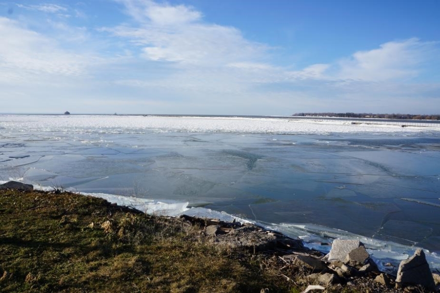 Somewhat broken sheets of ice cover a body of water.