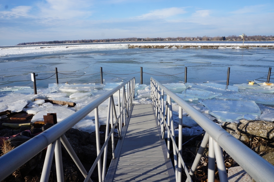 A view down the gangway of a ramp to a dock that is covered in broken sheets of ice and an icy canal