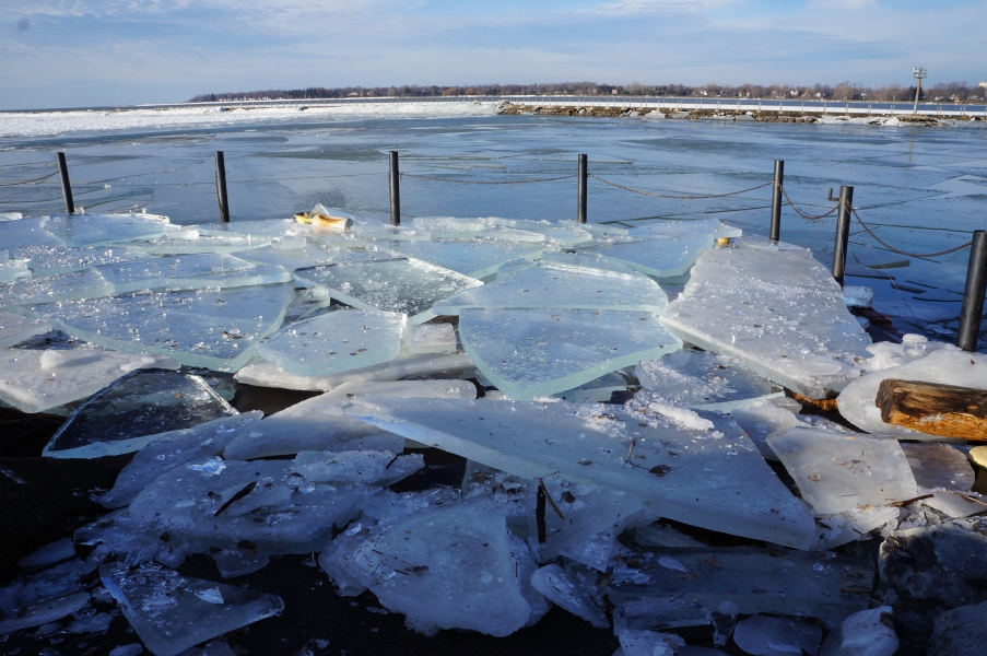 A boat dock covered with broken sheets of ice. Light sparkles in smaller pieces of ice. The sheets of ice are at least 4 inches thick.