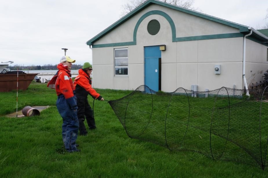 Two students in flotation suits hold a conical trap net open while standing on grass in front of a building.