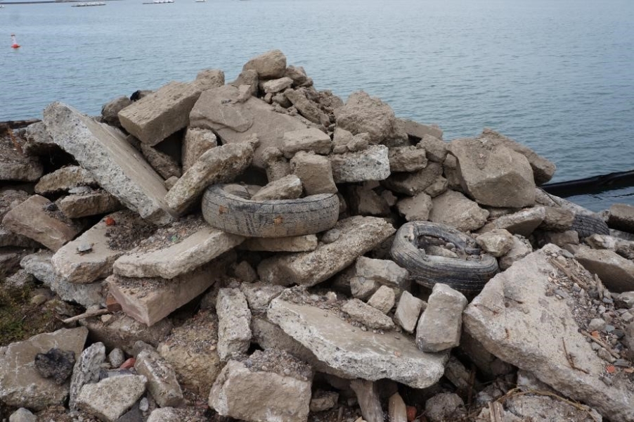 A pile of rocks, concrete debris, and tires by the waterfront.