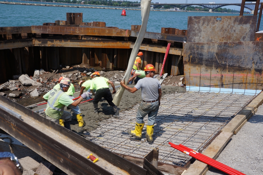 A construction crew working on laying cement on a frame. The construction area is bordered by a steel wall that holds out water.