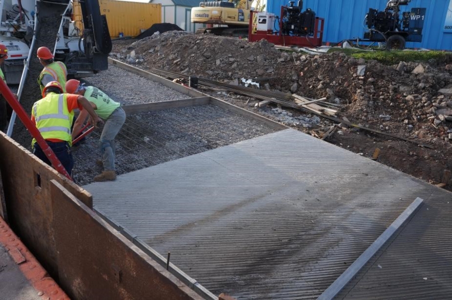 Construction workers working on a slope. The top of the slope has gravel and rebar but the lower portions have freshly cured cement.