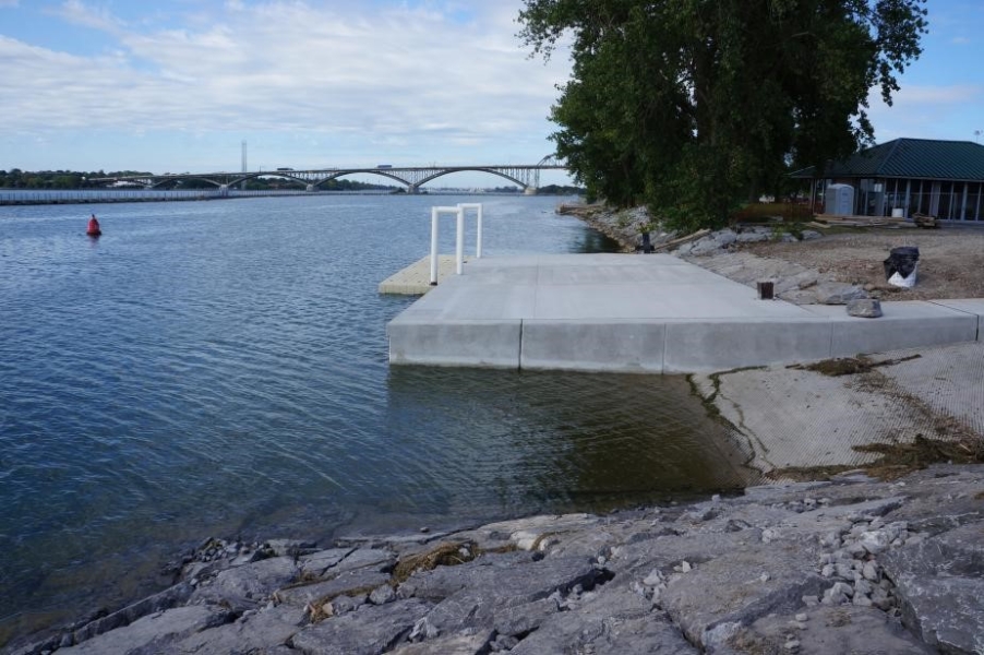 View of a boat launch and concrete dock with attached floating dock. Neat stones line the revetment in the foreground.