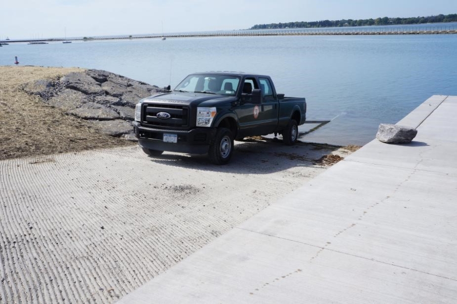 A pickup truck with a trailer backed into the water at a boat launch.