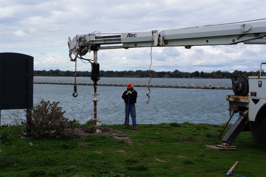 A worker watches an auger drill a hole in the ground near the waterfront.