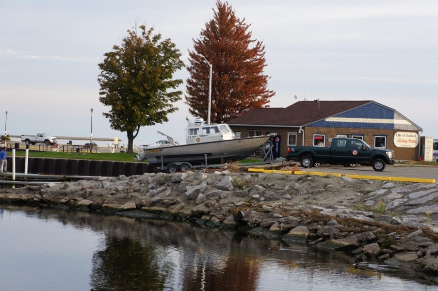 A truck backing a boat down a ramp at a boat launch during autumn.