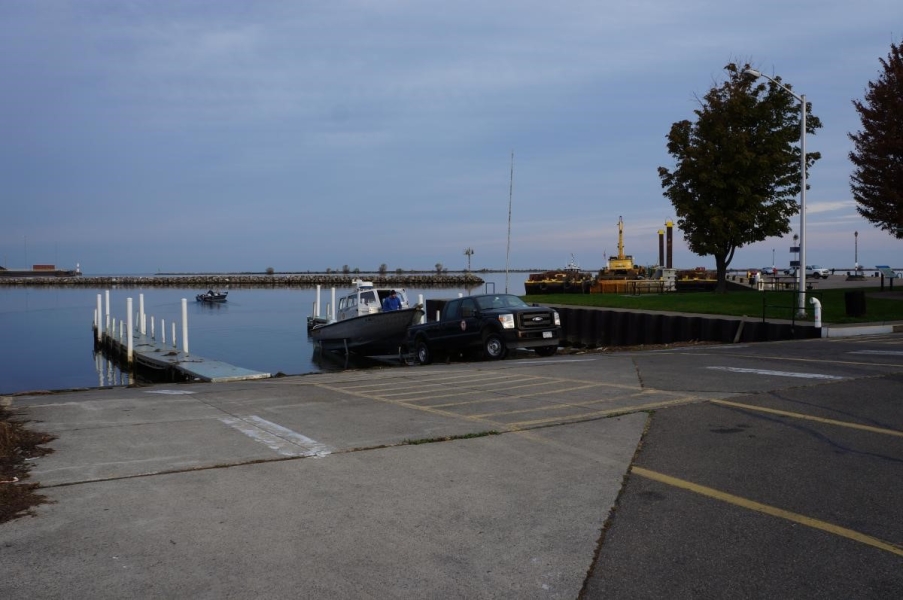 A truck and boat backed down a boat ramp to launch. A person is on the boat getting ready to launch.