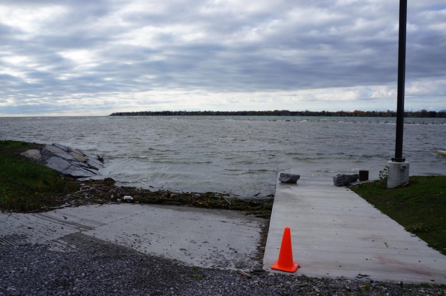 A ramp leading down the water is mostly submerged by waves. There is a line of weeds, wood, and garbage at the waterline.