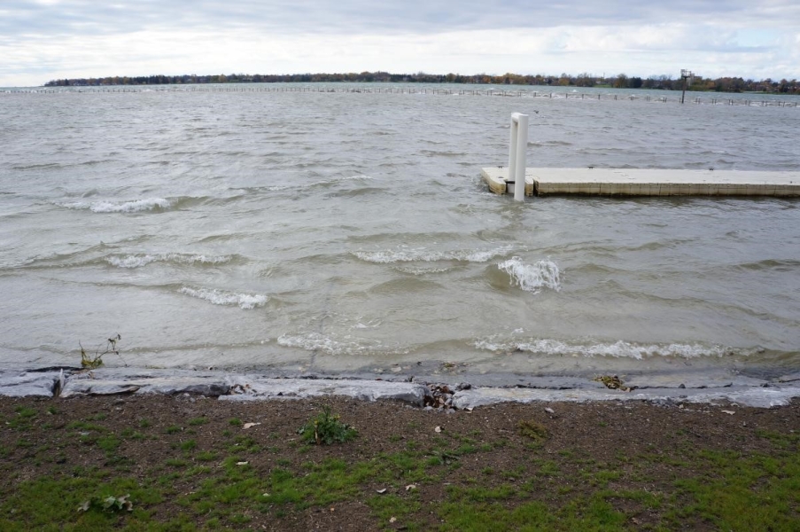 Water laps near the top of the stone barrier at the water's edge. A dock floats behind the water.