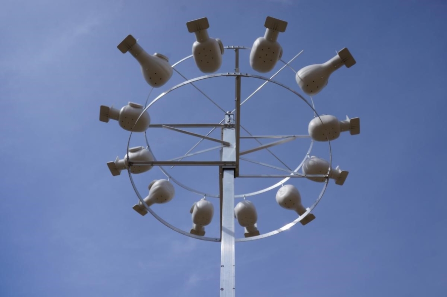 Twelve round bird houses in a ring around a pole, against a clear sky.