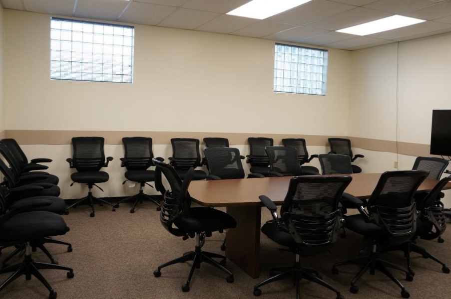 A conference room with computer chairs around a wooden table and along the walls.