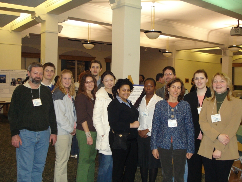 twelve people stand for a group photo inside a hall, with some posters on easels in the background