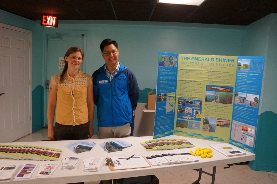 Two people stand behind a table with a poster and handouts.