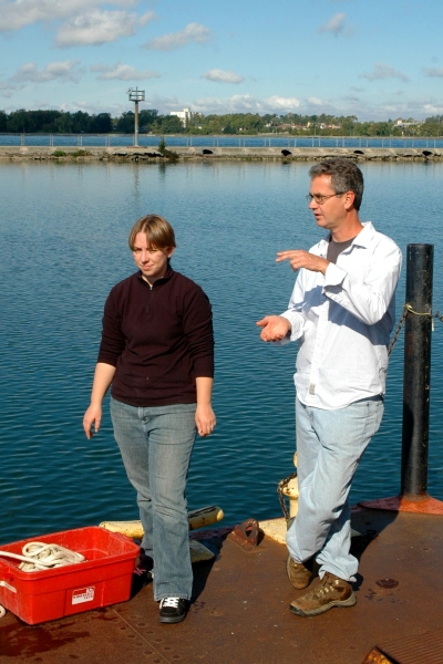 Two people stand on a dock by the water