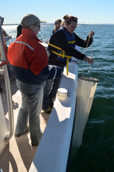 A person pulls up a long narrow conical net over the side of a boat while another person watches.