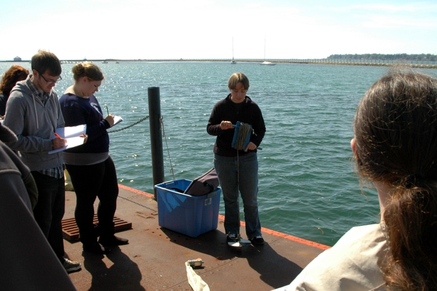 A group of people take notes as someone holds a coil of rope with a disk at the end of it