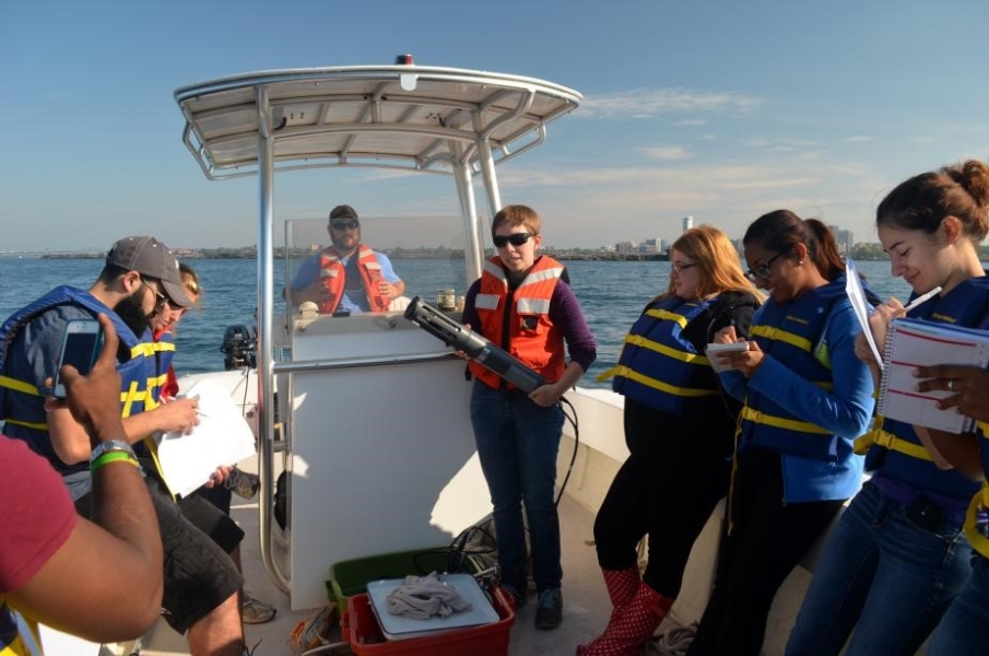 A class on a boat. One person stands at the control while another holds up a cylindrical instrument with a cable.