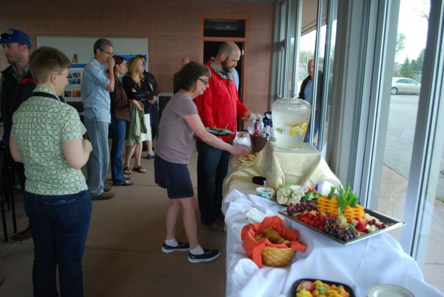 People grab food from a buffet table set up along a wall of windows