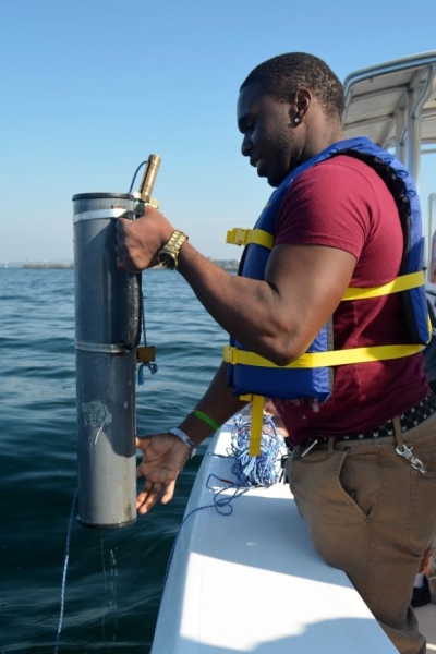 A student stands by the edge of the boat, holding a plastic cylinder over the water.