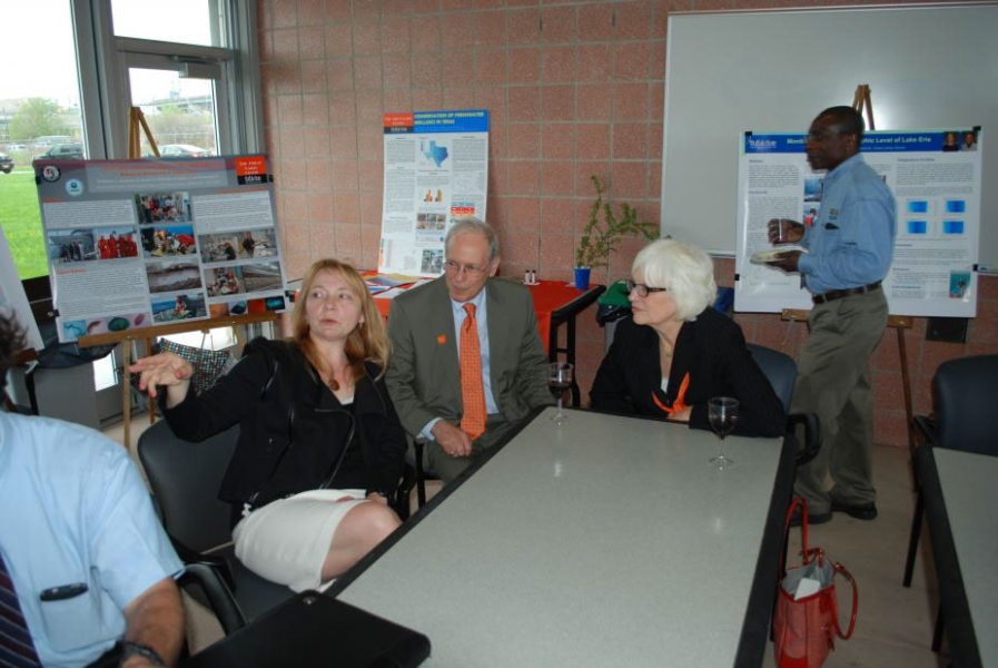 A few people sit at a table. There are posters on easels behind them.