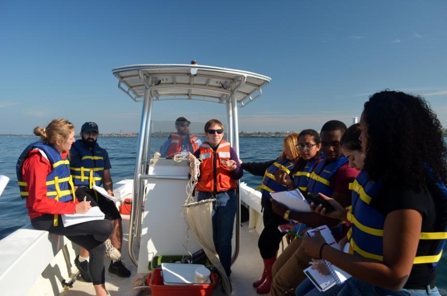 A class on a boat. One person stands at the control while another holds up a conical fine-mesh net.