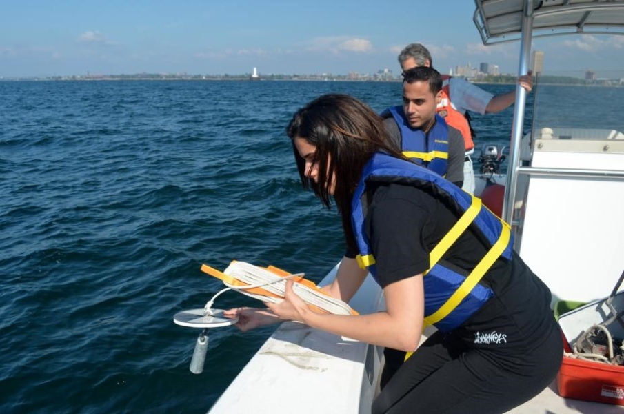 A student leans over the side of the boat to lower a disk with a weight hanging from it.