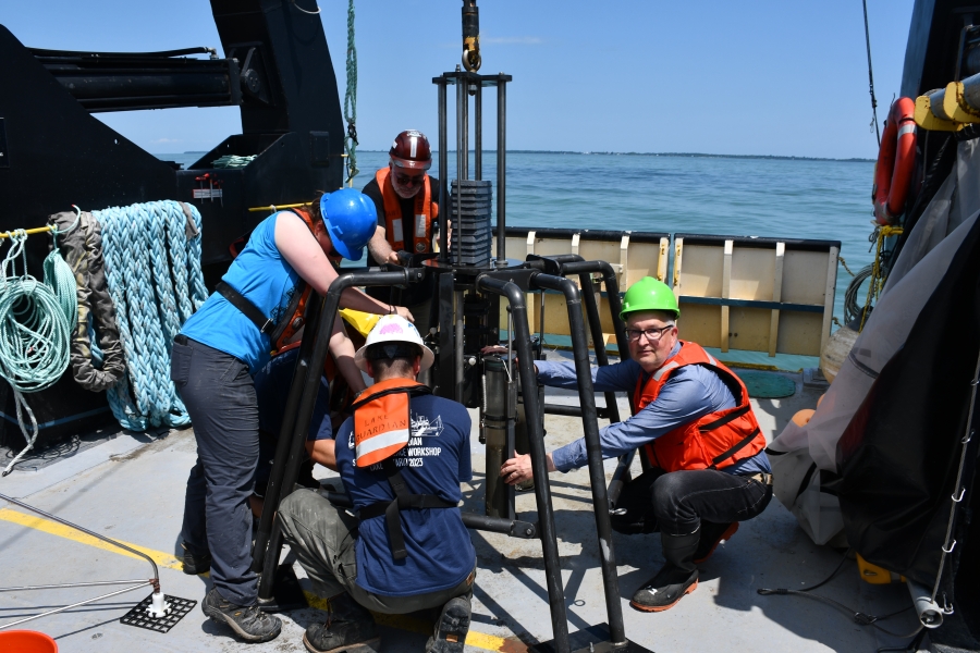 Four people on the deck of a boat work on a piece of equipment to remove sediment cores