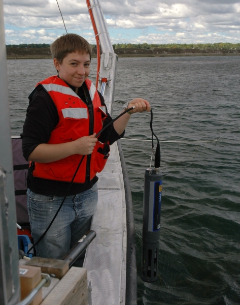 A person on a boat smiles as they lower a research instrument over the side of the boat