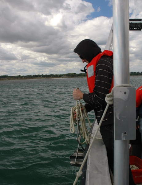 a student at the edge of the boat pulls up rope and sampling equipment