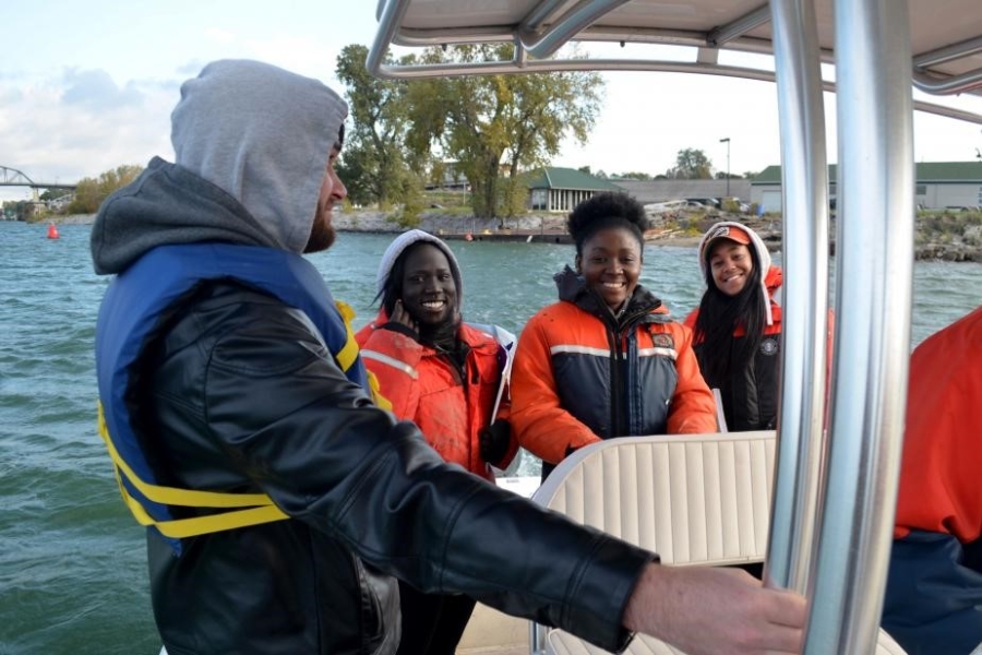 People on a boat. Three are seated and smiling at the camera, while one stands holding a railing.