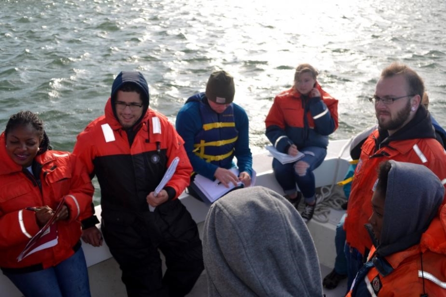 People wearing cold water safety gear on a boat. Some are taking notes.